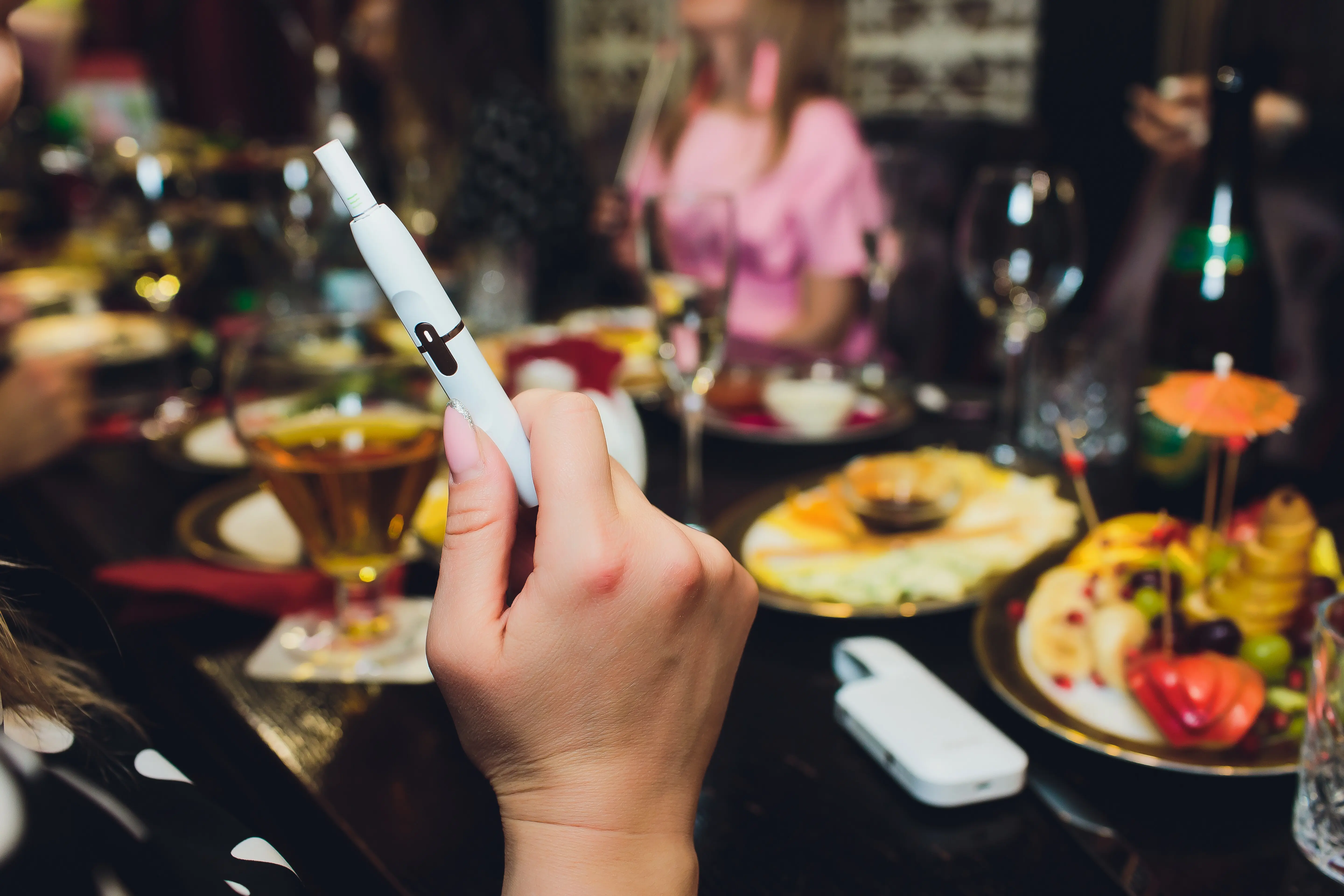 Heat‑not‑burn tobacco product technology, with a woman holding an e‑cigarette in her hand before smoking.