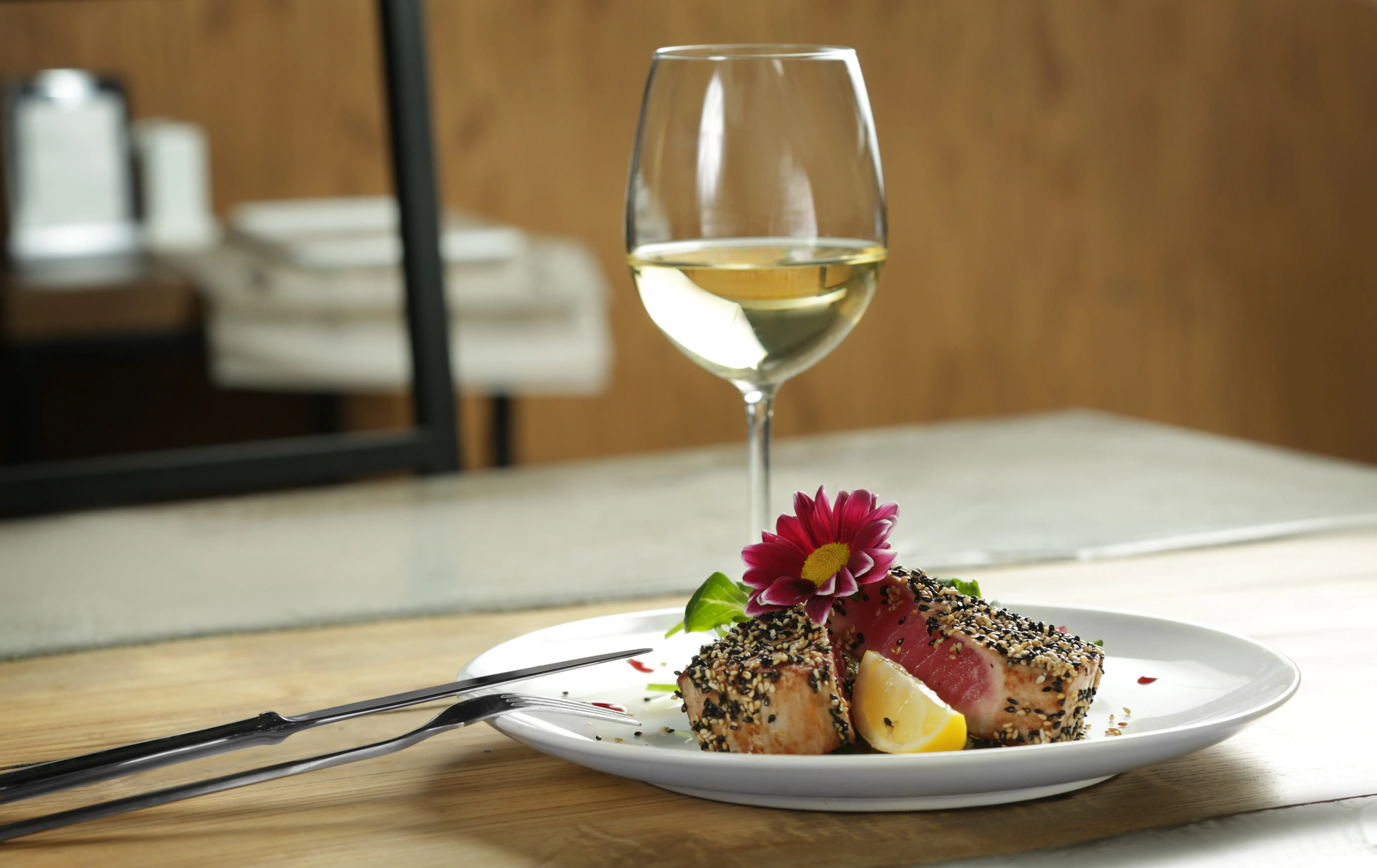 A plate with a delicious tuna fillet and a glass of wine on a table
